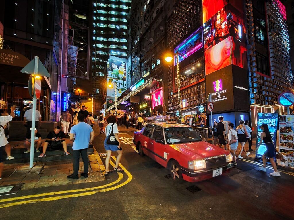Persone camminano vicino ad un'auto rossa a Lan Kwai Fong