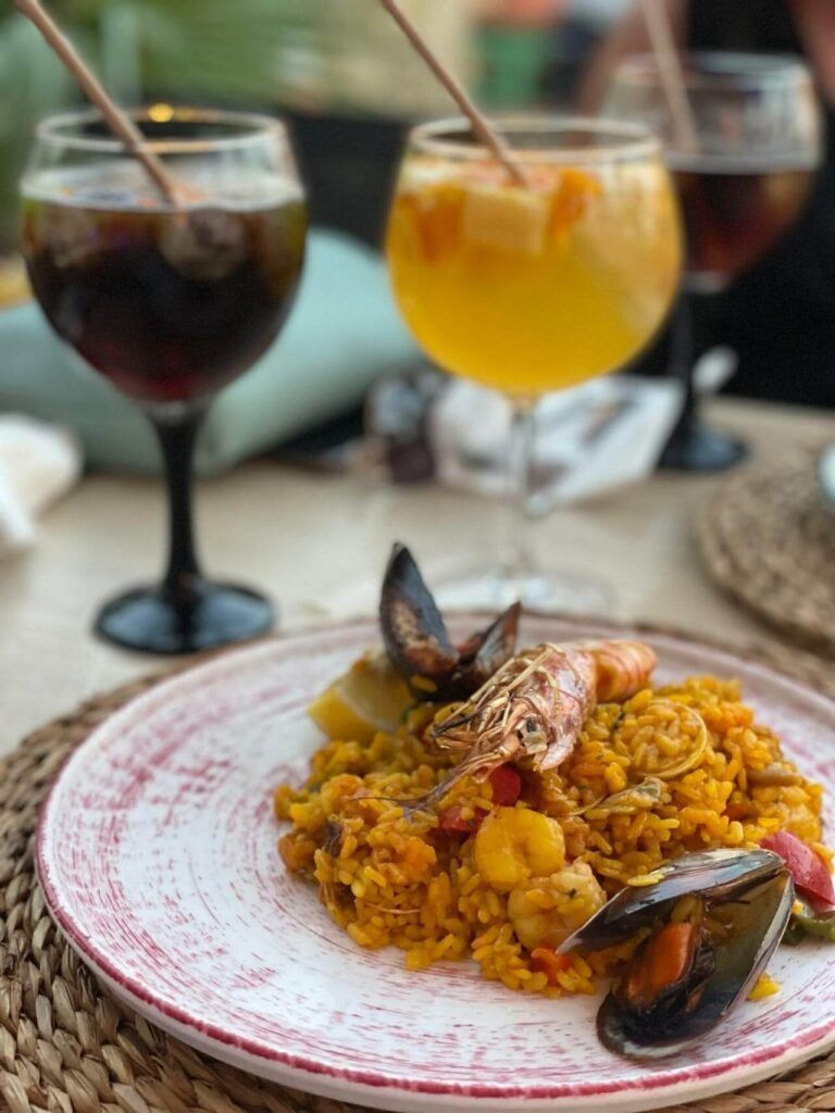 Un piatto di paella e due bicchieri con cocktail sullo sfondo