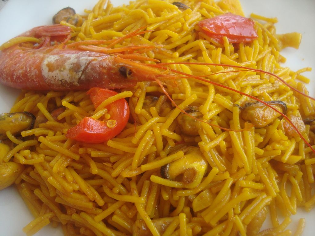 Un piatto di fideuà, una tradizionale paella di pasta, con gamberi, cozze e pomodori