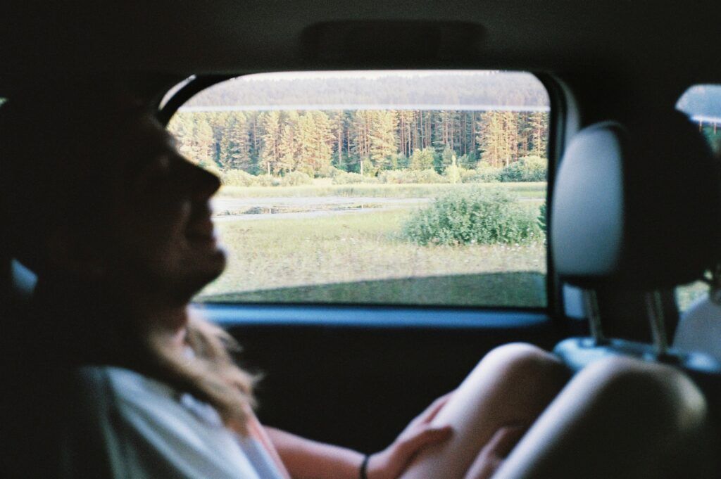 Persona seduta sul sedile posteriore di un’auto, con vista sul paesaggio naturale e una foresta al tramonto attraverso il finestrino.