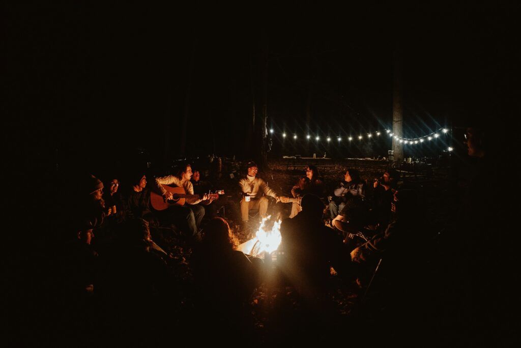 Serata intorno al fuoco con un gruppo di viaggiatori, musica dal vivo con chitarra e atmosfera chill.