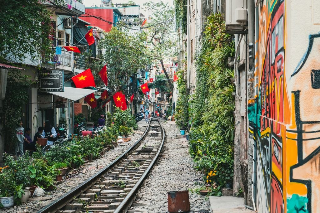La celebre Train Street di Hanoi, con i binari che tagliano le case colorate e bandiere vietnamite che sventolano tra caffè e murales.
