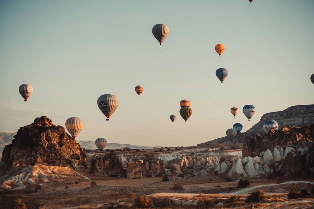 Decine di mongolfiere sorvolano i camini delle fate in Cappadocia, illuminate dalla luce calda del tramonto.