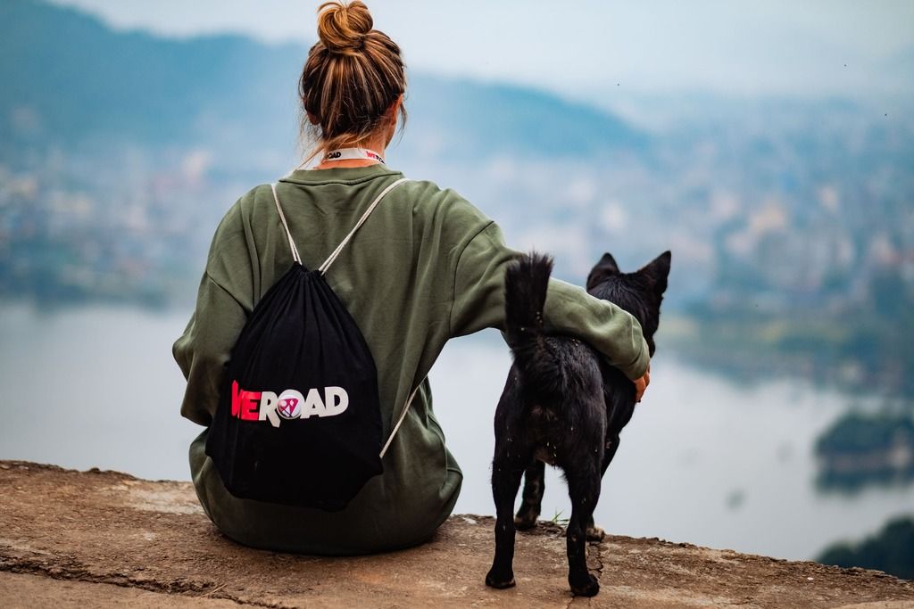 Viaggiatrice con zaino WeRoad e cane, affacciata su Pokhara: panorami mozzafiato e libertà nelle valli del Nepal.