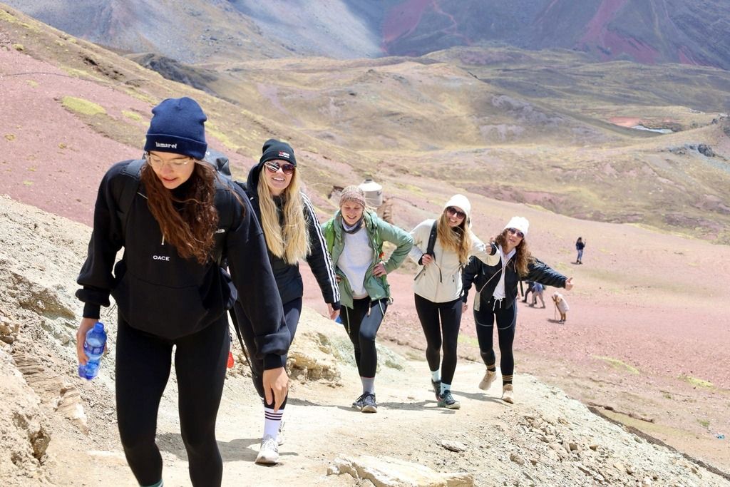 Gruppo WeRoad di ragazze in salita lungo il sentiero verso Vinicunca, tra risate, vento in faccia e panorami mozzafiato delle Ande peruviane.