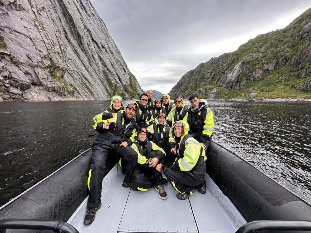 Gruppo di viaggiatori WeRoad su gommone durante un’escursione nei fiordi norvegesi, circondati da pareti rocciose e paesaggio verde