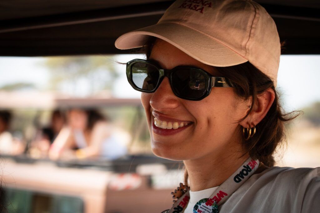 Viaggiatrice WeRoad sorride all'interno di un fuoristrada, indossando occhiali da sole e cappellino.