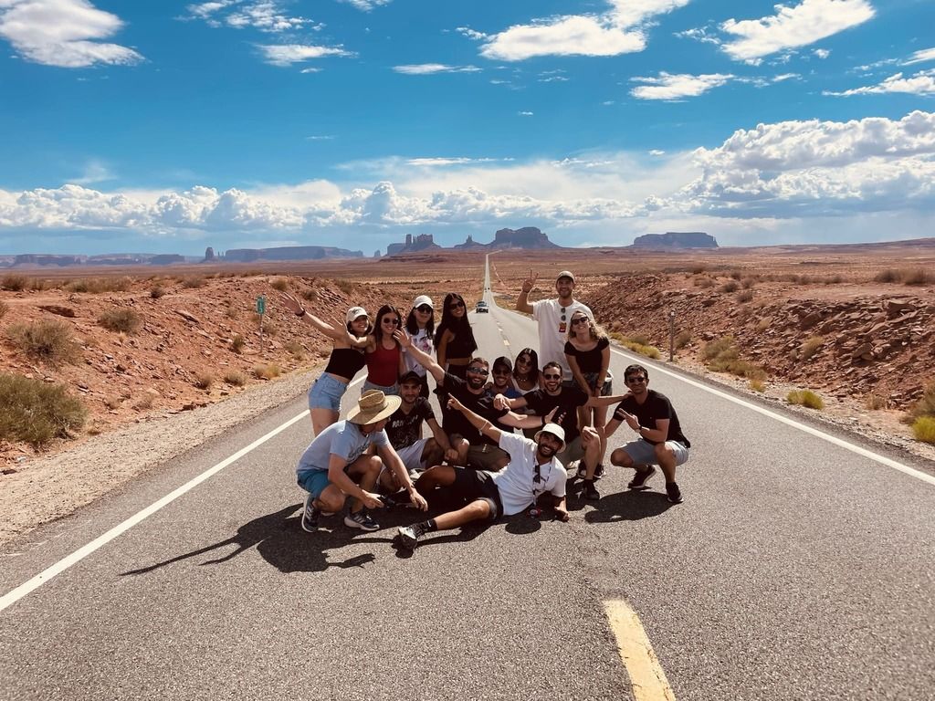 Un gruppo WeRoad al centro di una lunga strada dritta con il paesaggio desertico tipico del Far West americano. 