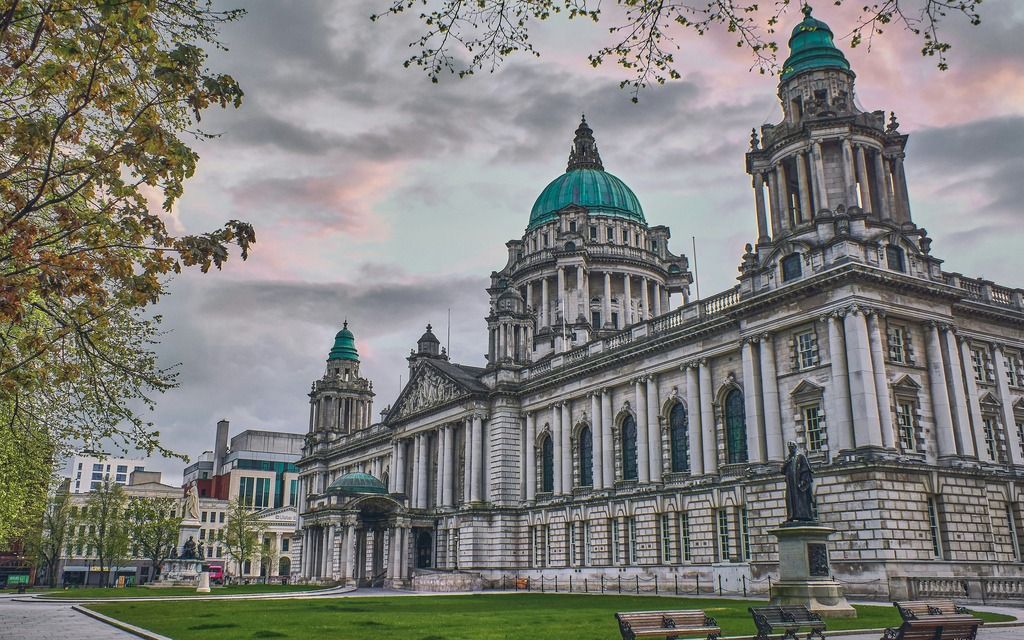 Facciata monumentale di un edificio storico di Belfast con cupole verde rame al tramonto.