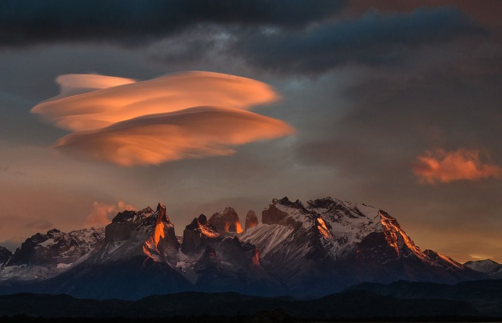 Catena montuosa della Patagonia con cime innevate illuminate dal sole al tramonto e nuvole spettacolari in cielo.