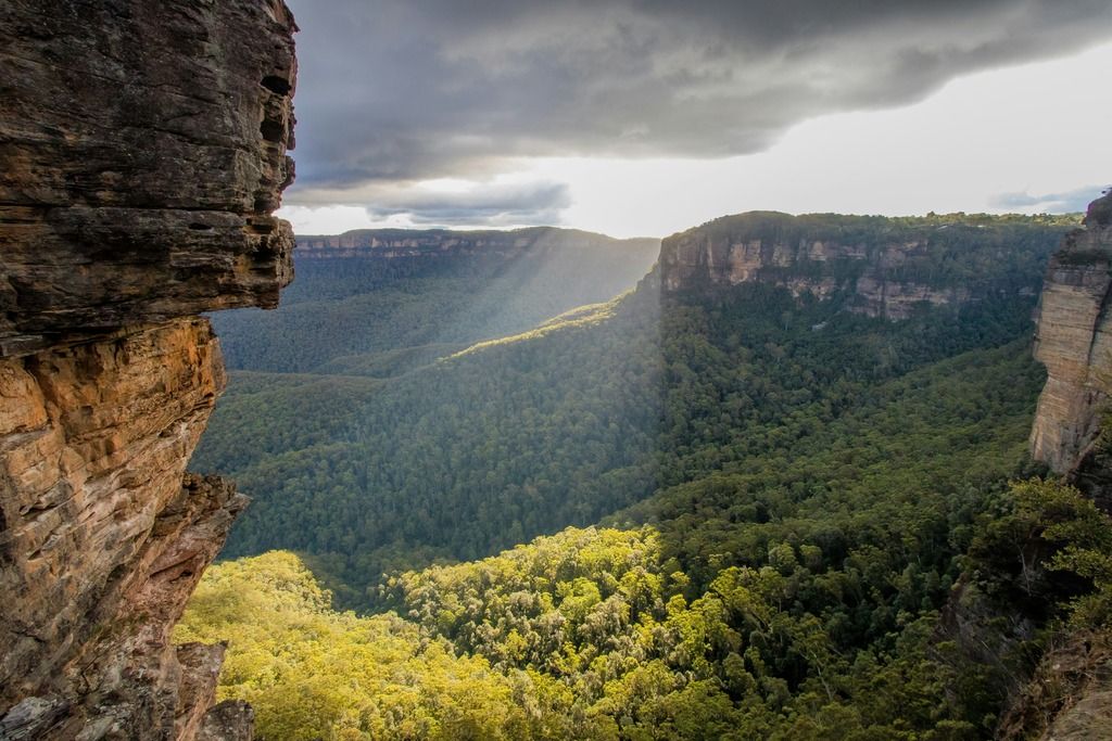 Panorama delle Blue Mountains in Australia, con foresta verde e raggi di sole che filtrano tra le nuvole.