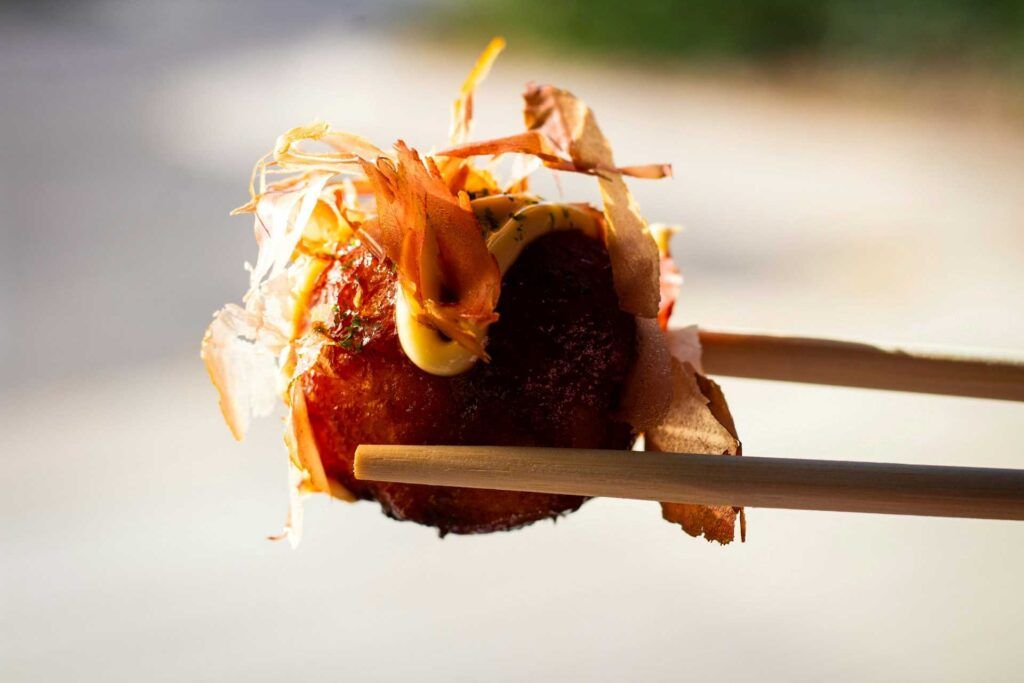 Un Takoyaki (palline di pastella con polpo) sorretto dalle bacchette.