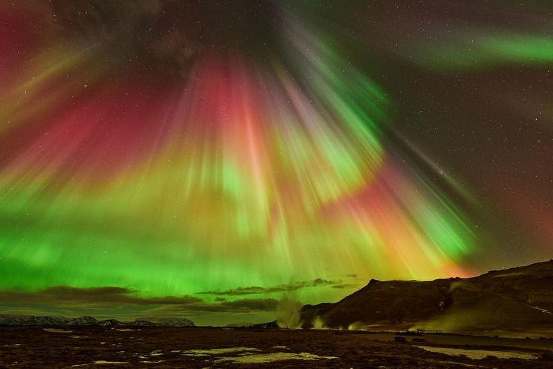 Aurora boreale con striature rosse, verdi e gialle nel cielo notturno sopra un paesaggio montano innevato