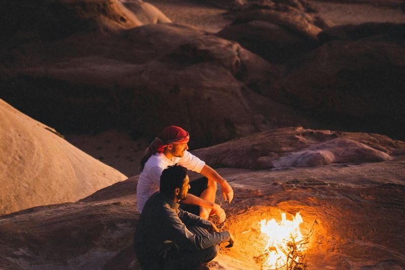 Due persone sedute attorno a un falò tra le rocce del deserto di notte, Wadi Rum in Giordania