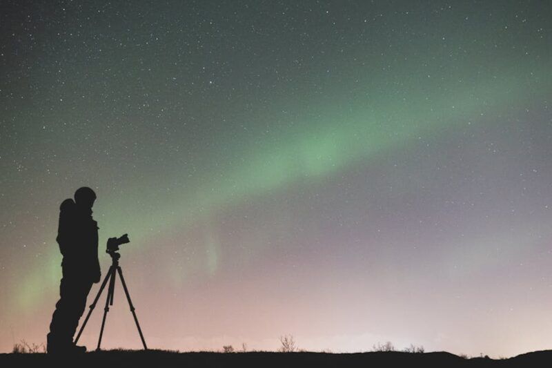 Silhouette di un fotografo con treppiede che ritrae l'aurora boreale verde nel cielo stellato notturno