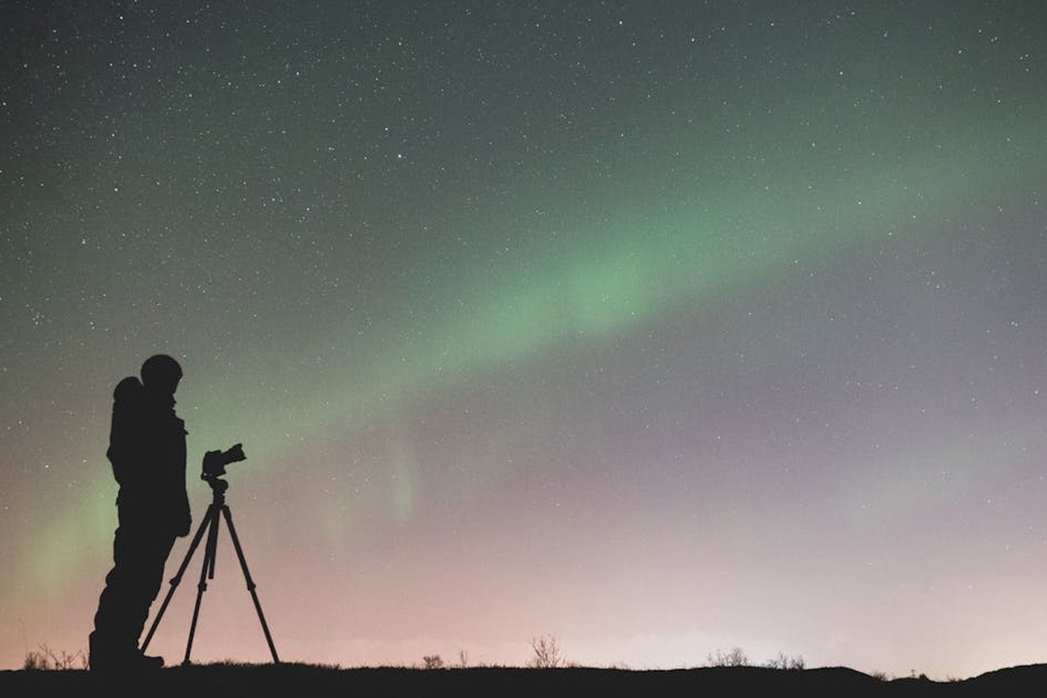Silhouette di un fotografo con treppiede che ritrae l'aurora boreale verde nel cielo stellato notturno