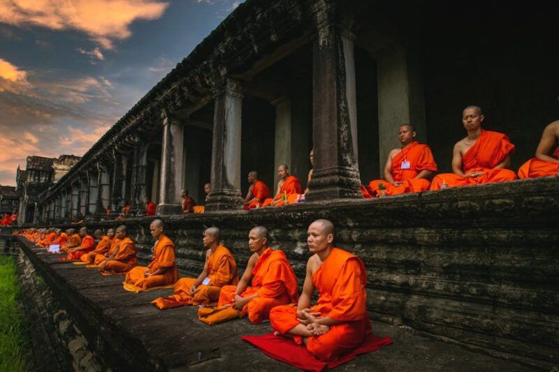Fila di monaci buddisti in veste arancione in meditazione sulle terrazze del tempio di Angkor Wat, Cambogia, al tramonto