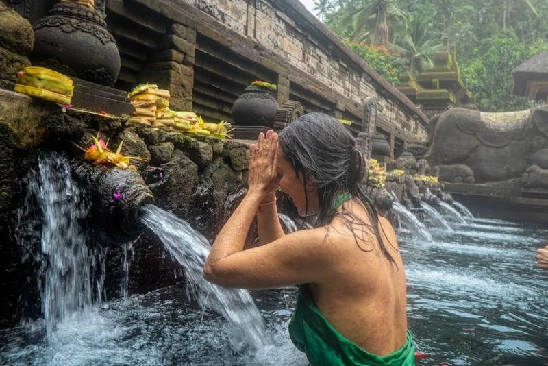 Donne durante il rituale di purificazione nelle acque sacre del tempio Tirta Empul a Bali, Indonesia, con offerte floreali sullo sfondo