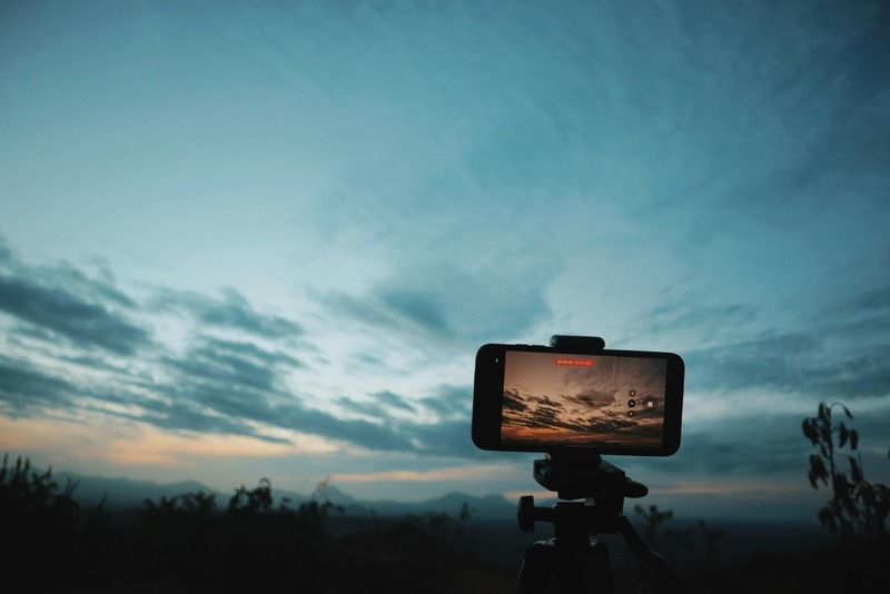 Smartphone su treppiede che registra un cielo nuvoloso al tramonto su un paesaggio di montagna