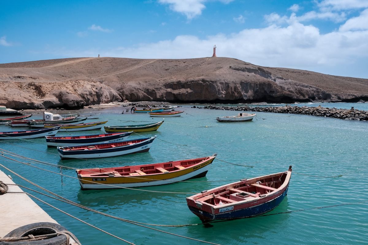 Barche da pesca colorate ormeggiate in acque calme davanti alla costa arida di Pedra Lume