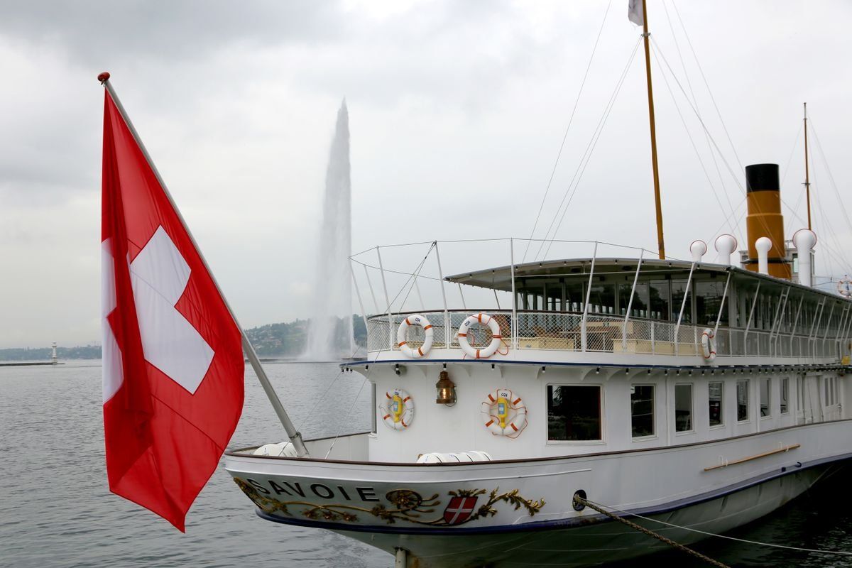 Battello a vapore con bandiera svizzera sul lago e getto d'acqua sullo sfondo
