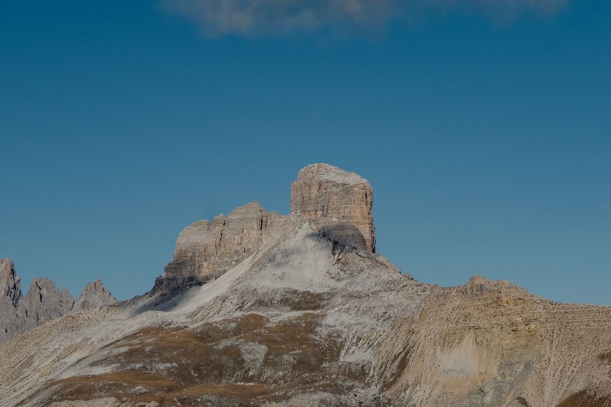 Cima rocciosa isolata delle Dolomiti sotto cielo azzurro con pendii chiari e aridi