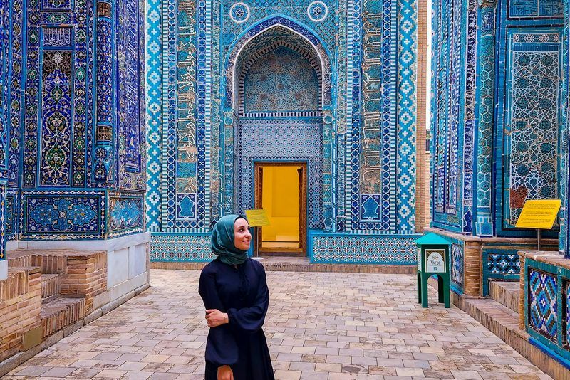 Donna con hijab e abito lungo davanti al portale in mosaico turchese del mausoleo Shah-i-Zinda a Samarcanda