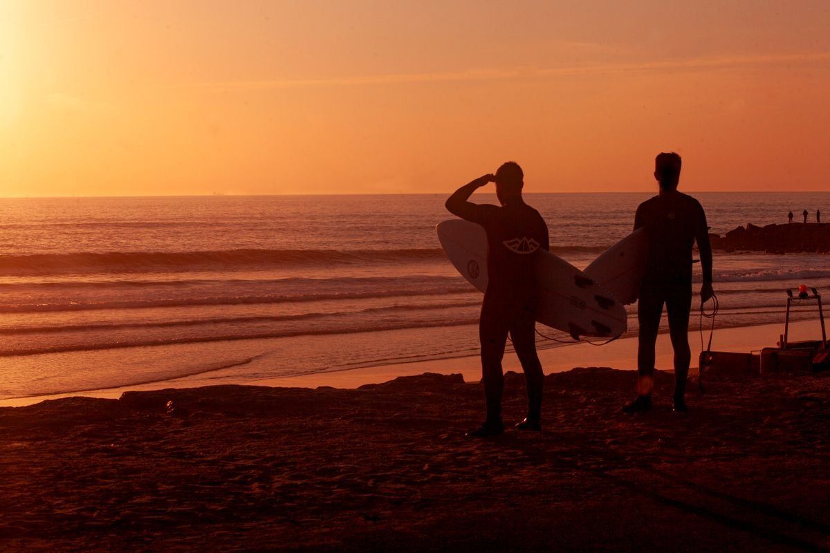 Due surfisti in controluce con tavole sulla spiaggia al tramonto