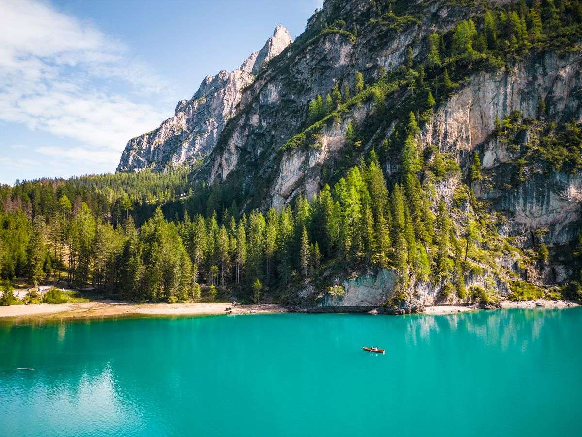 Lago turchese tra bosco fitto e pareti rocciose alpine