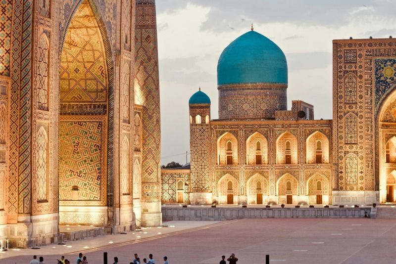 Piazza Registan a Samarcanda illuminata al tramonto con la cupola turchese e visitatori in controluce