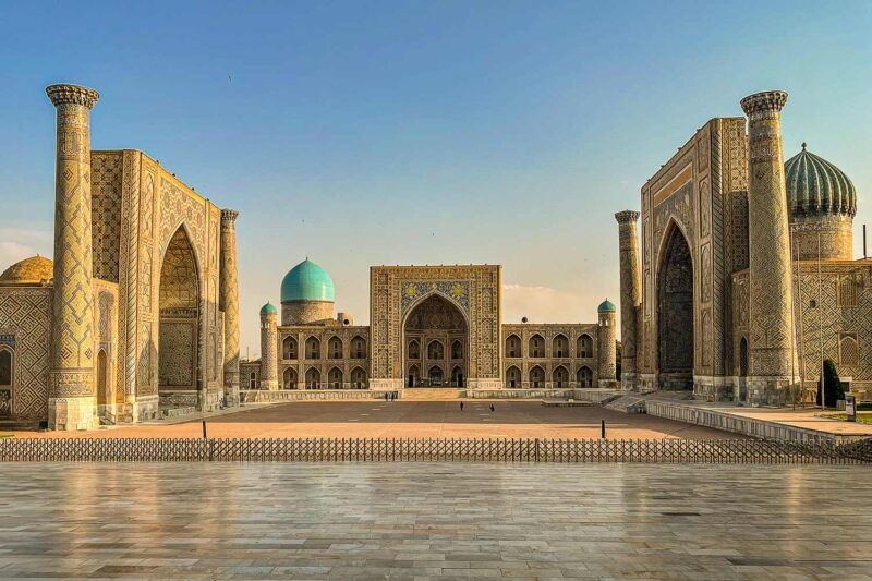 Piazza Registan a Samarcanda con le tre madrase in pietra dorata e la cupola turchese sotto un cielo azzurro terso