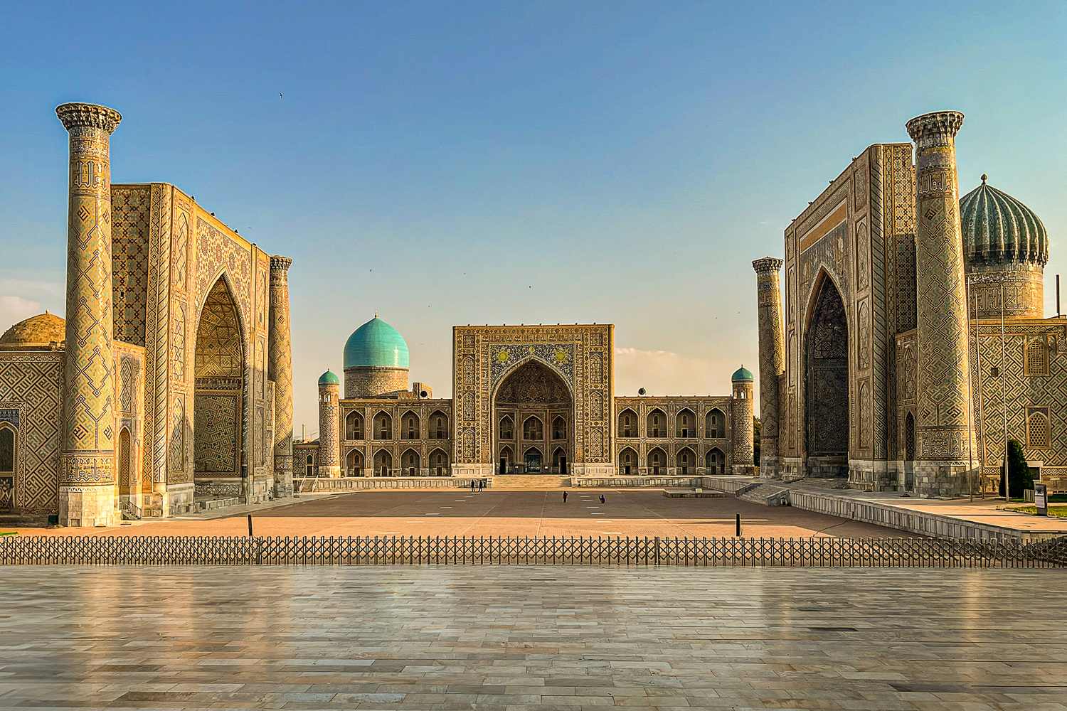 Piazza Registan a Samarcanda con le tre madrase in pietra dorata e la cupola turchese sotto un cielo azzurro terso