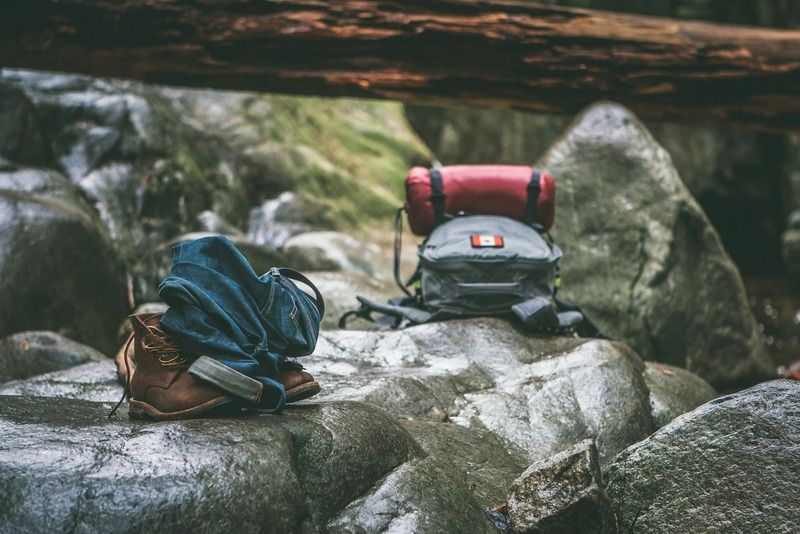 Scarponi da trekking, jeans arrotolati e zaino da campeggio appoggiati su rocce nel bosco