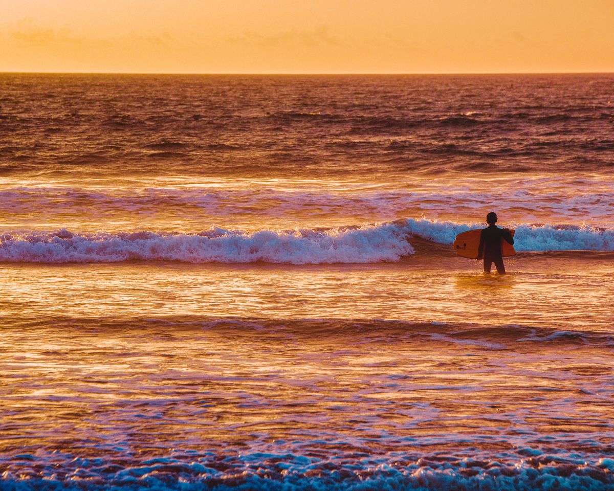 Surfista in piedi nell'acqua al tramonto con tavola sotto il braccio