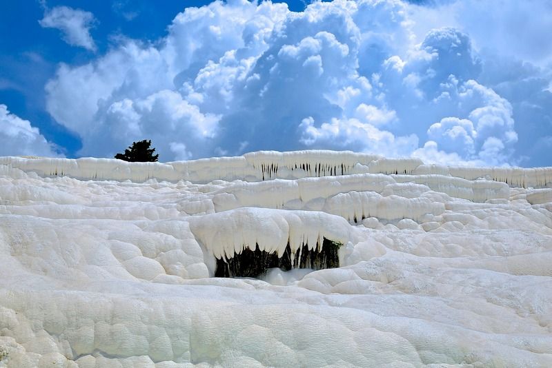 Formazioni calcaree bianche di Pamukkale contro un cielo drammatico con nuvole e un albero solitario