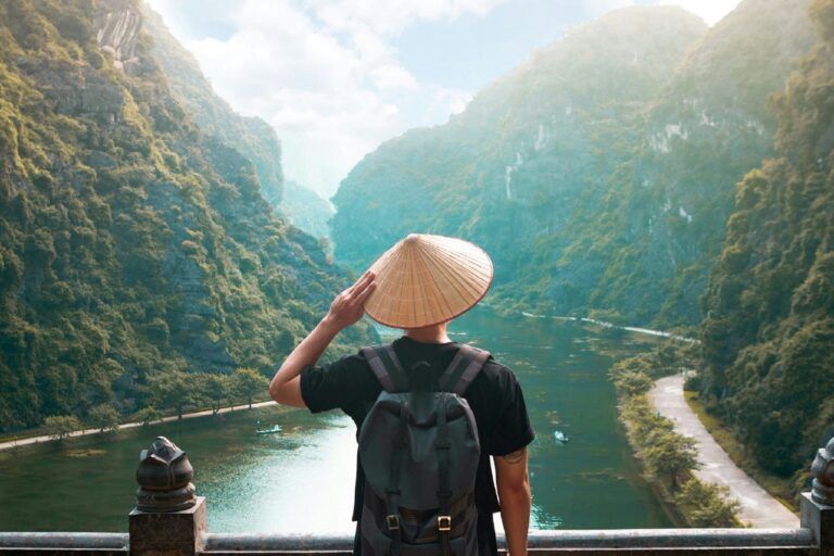 Viaggiatore di spalle con cappello conico vietnamita ammira la valle carsica di Trang An in Vietnam