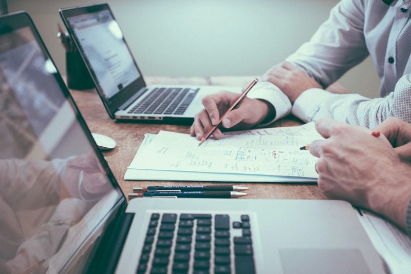 Consulente scrive appunti su documenti e grafici accanto a due laptop aperti su una scrivania