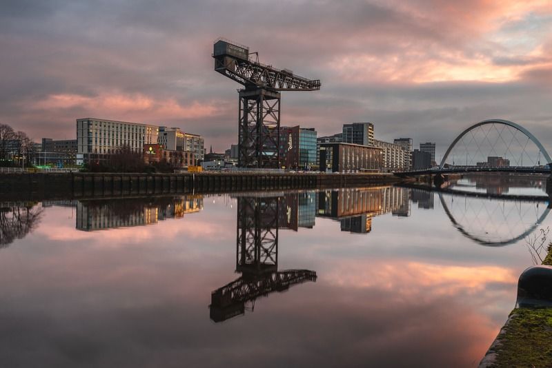 La gru Finnieston si riflette nelle acque calme del fiume Clyde a Glasgow al tramonto, con il Clyde Arc sullo sfondo