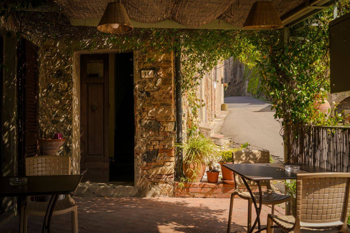 Patio con tavoli accanto a una casa in pietra e strada stretta tra muri rustici