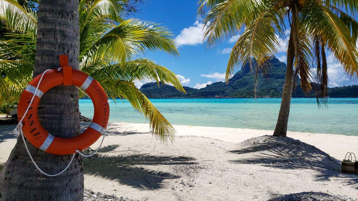 Salvagente appeso a una palma su spiaggia bianca con laguna turchese e montagne