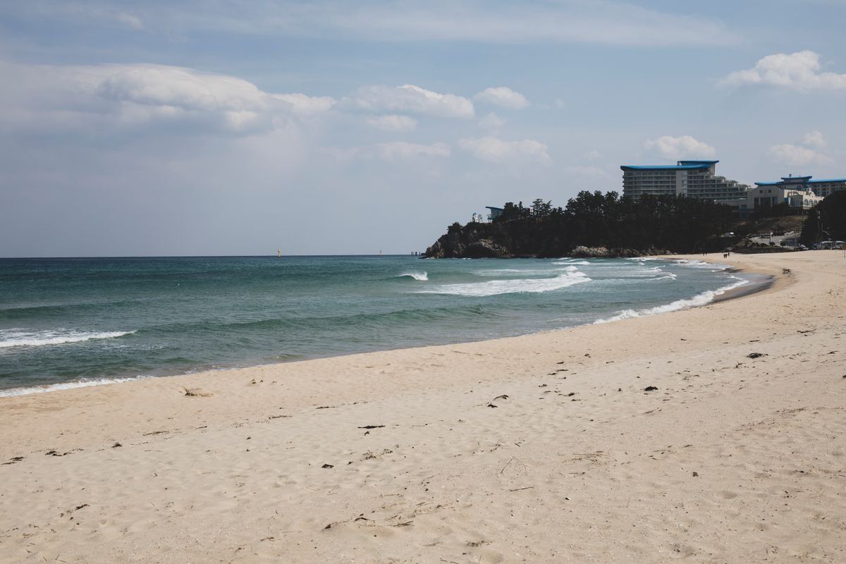 Spiaggia sabbiosa con onde leggere, cielo nuvoloso ed edifici sul promontorio