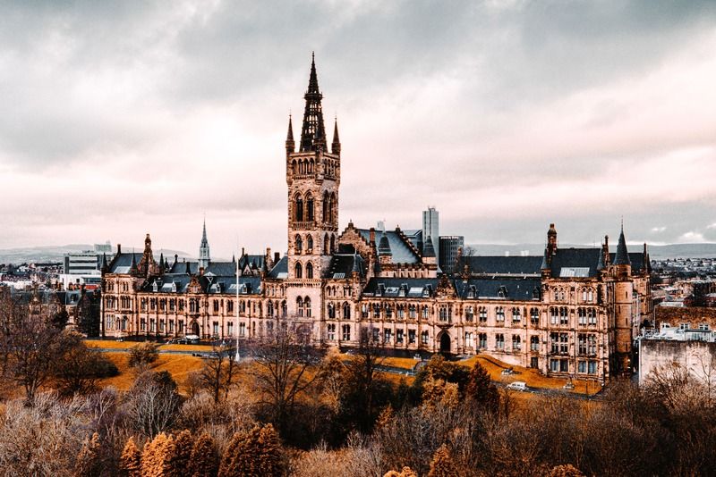 "Vista aerea della torre gotica dell'Università di Glasgow circondata da alberi autunnali sotto un cielo drammatico