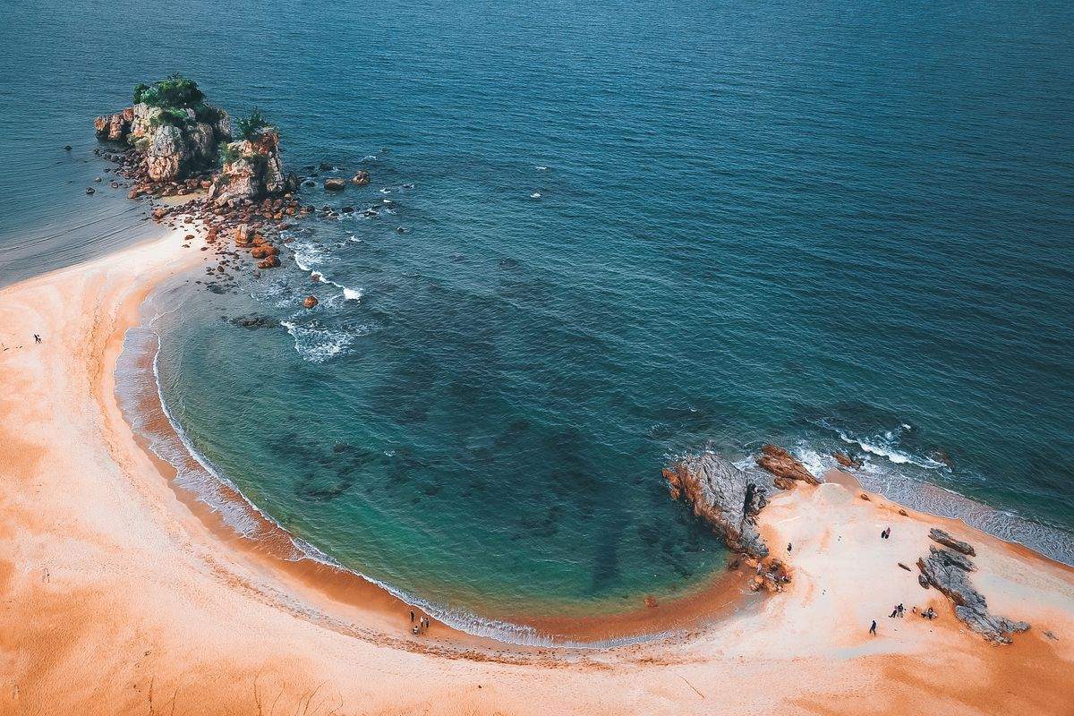 Vista dall’alto di una baia con sabbia chiara, acqua turchese e scogli affioranti