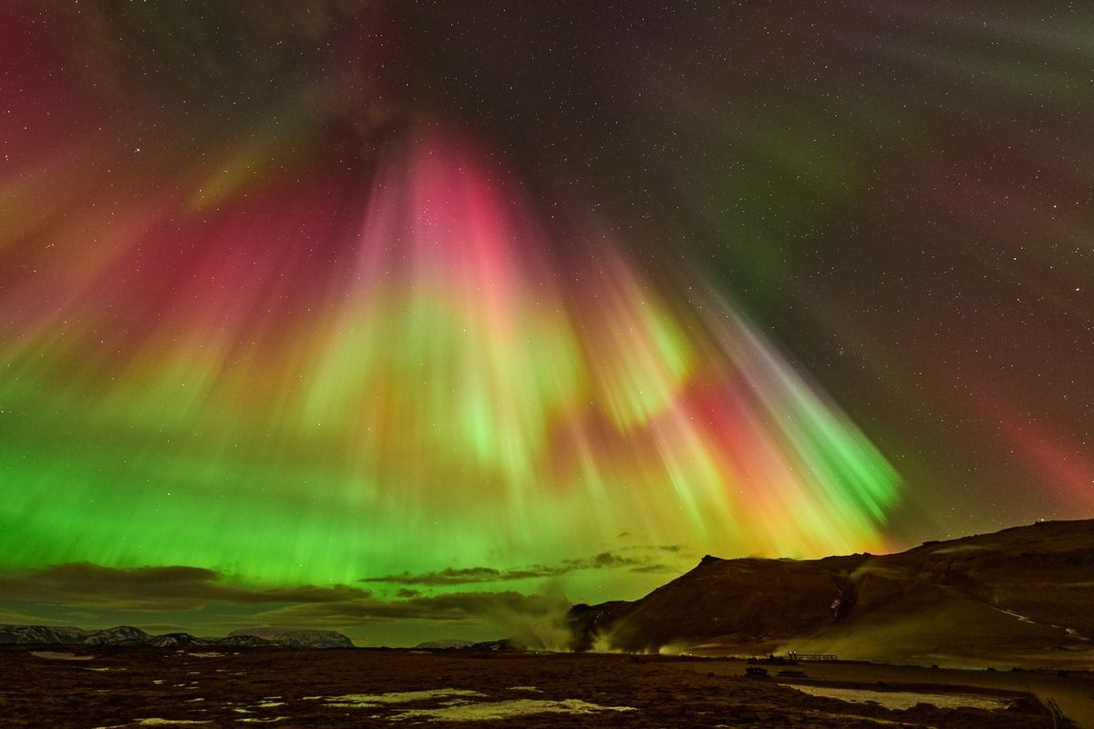 Aurora boreale verde e rosa sopra un paesaggio vulcanico sotto il cielo stellato