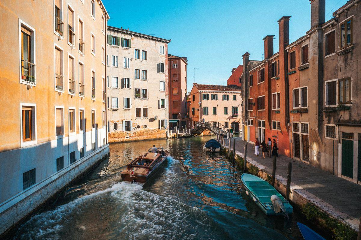 Canale di Venezia con barche in movimento tra palazzi colorati sotto il sole