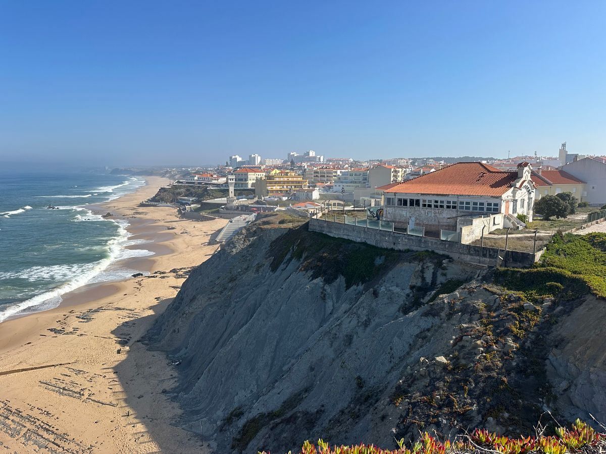 Case sul bordo della falesia sopra Praia das Maçãs con lunga spiaggia e oceano sotto cielo limpido