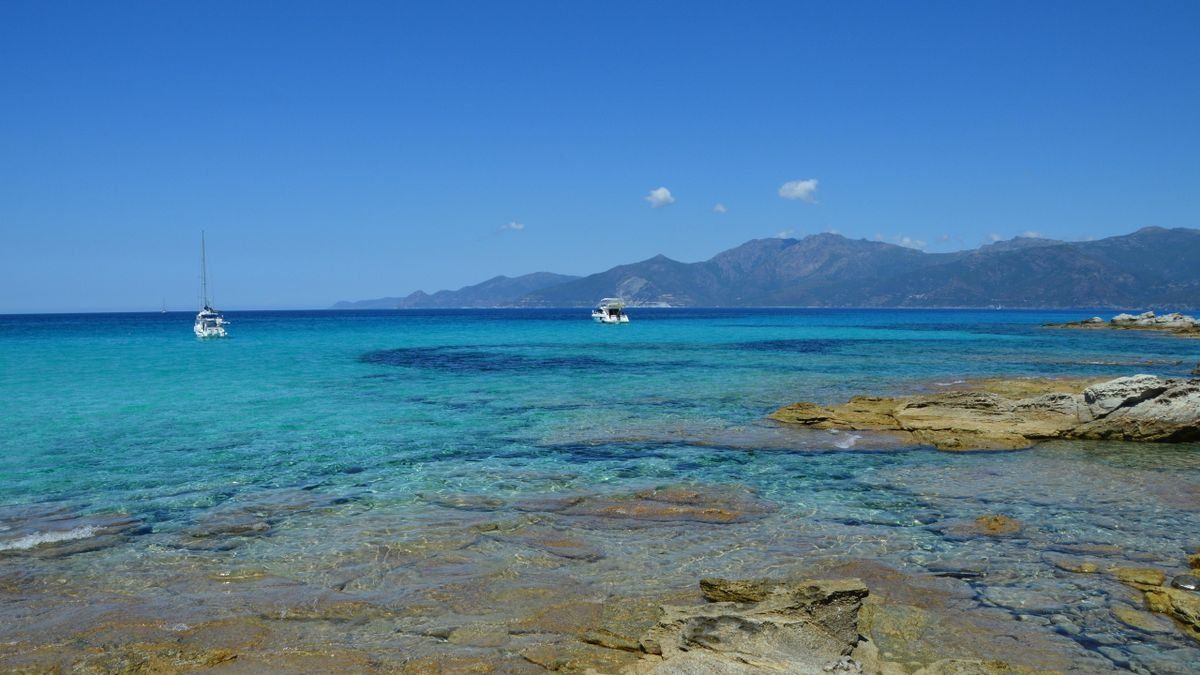 Costa rocciosa con acqua cristallina e due barche al largo sotto un cielo limpido