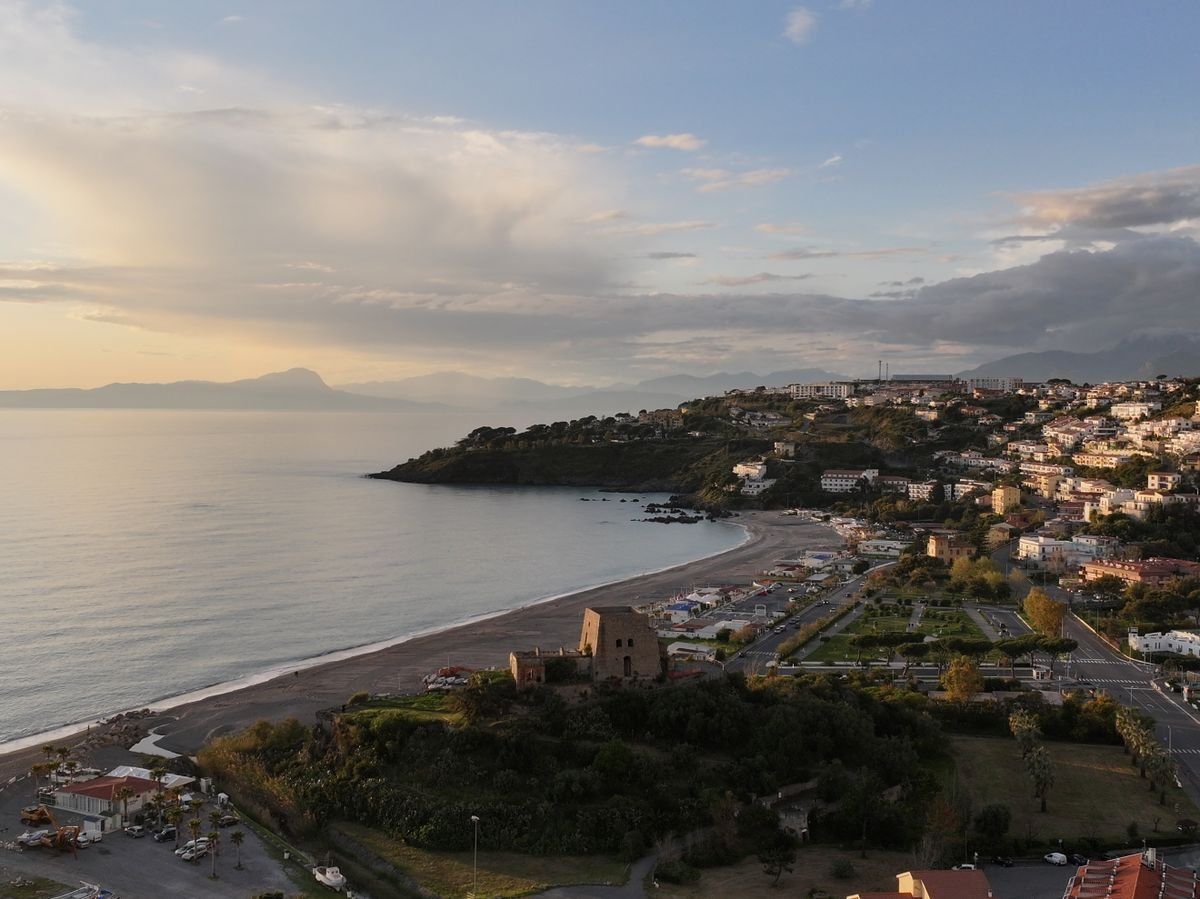 Panorama aereo di una cittadina costiera al tramonto con spiaggia, collina e case sul mare