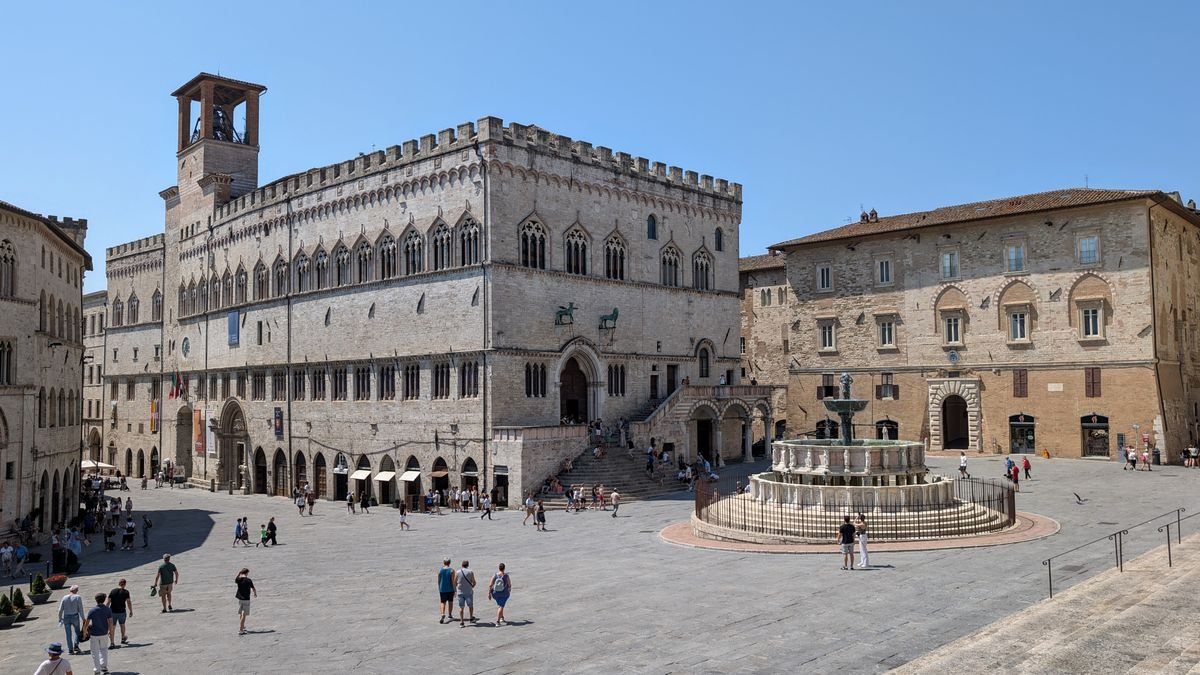 Piazza storica di Perugia con Palazzo dei Priori, fontana centrale e persone che camminano