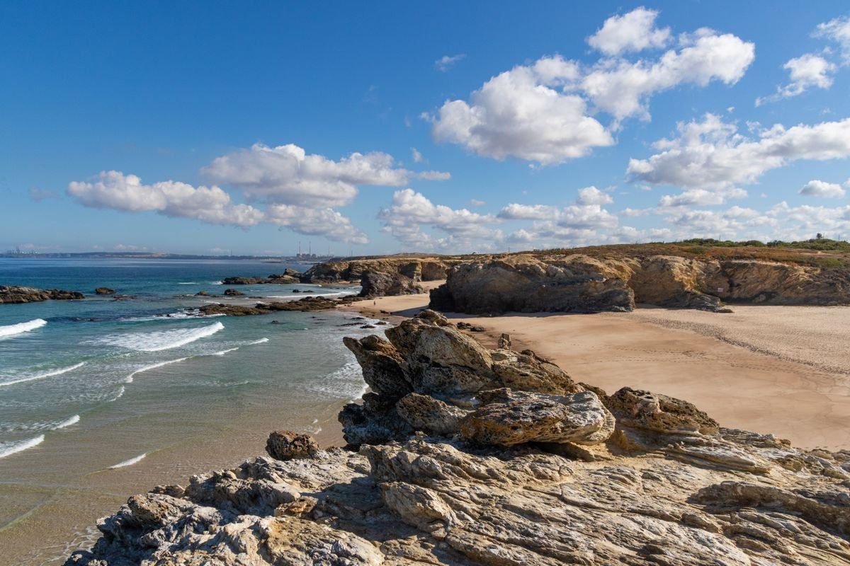 Scogliera rocciosa e spiaggia sabbiosa sull’oceano sotto un cielo azzurro con nuvole